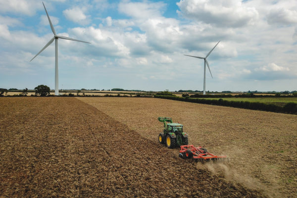 A tractor ploughing a field with wind turbines in the distance