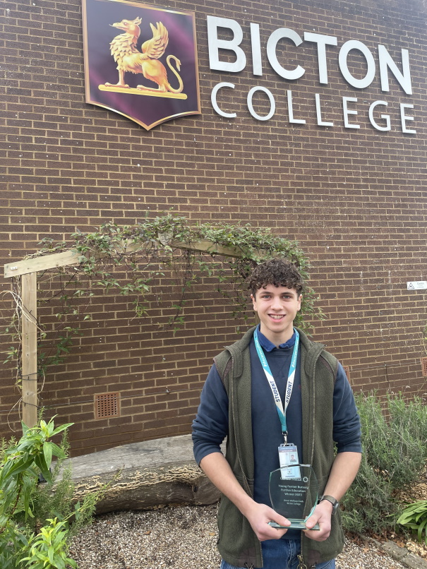 Agriculture student Oscar stood in front of red brick building with Bicton College logo on it holding a glass trophy